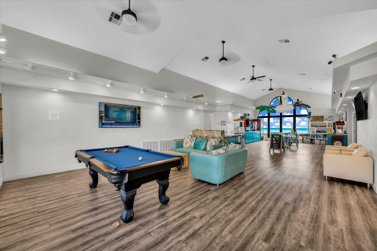 Spacious entertainment room featuring wood-finish flooring and a vaulted ceiling with multiple ceiling fans
