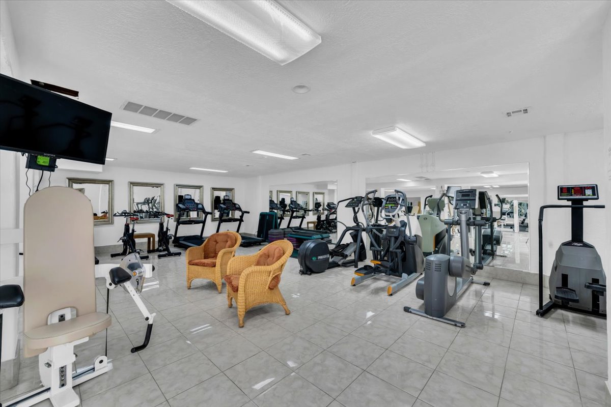 Fitness center featuring multiple exercise machines, mirrored walls, recessed lighting, and tile flooring