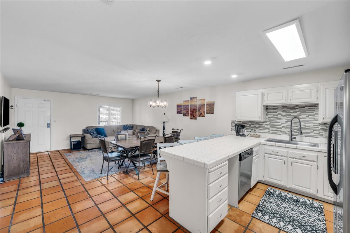 Spacious living area featuring terra cotta tile flooring, white kitchen cabinetry, a tiled kitchen backsplash, and stainless steel appliances