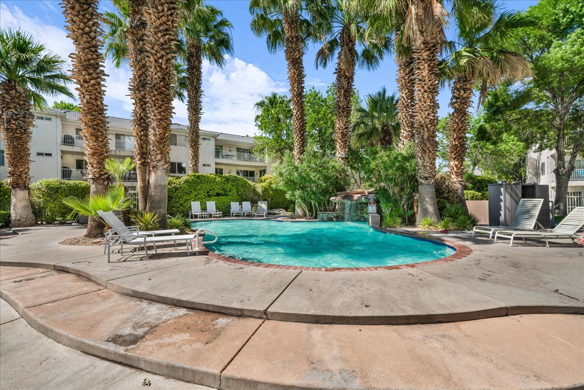 Resort-style pool area featuring numerous mature palm trees, a concrete pool deck, and a rock waterfall feature