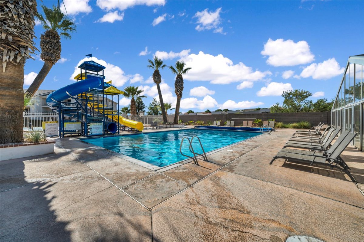 Swimming pool area featuring a multi-level water slide structure, multiple lounge chairs, and mature palm trees