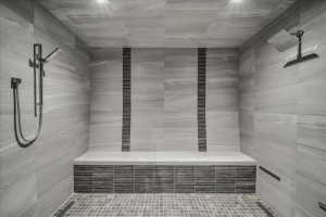 Spacious shower featuring full-height stone-look tile, a built-in bench, dual showerheads with a handheld sprayer, and mosaic tile accents