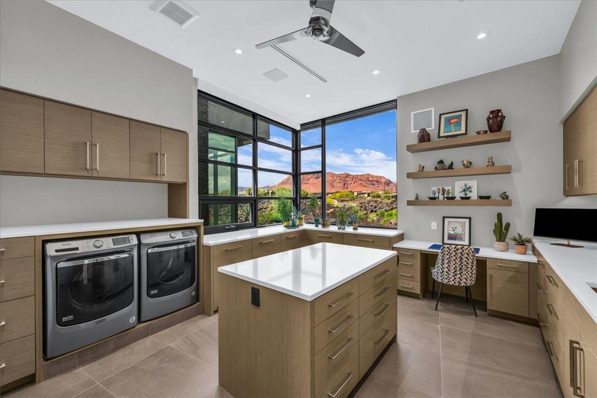 Utility room featuring a built-in washer and dryer, extensive cabinetry with light wood-finish, stone countertops, and a central island