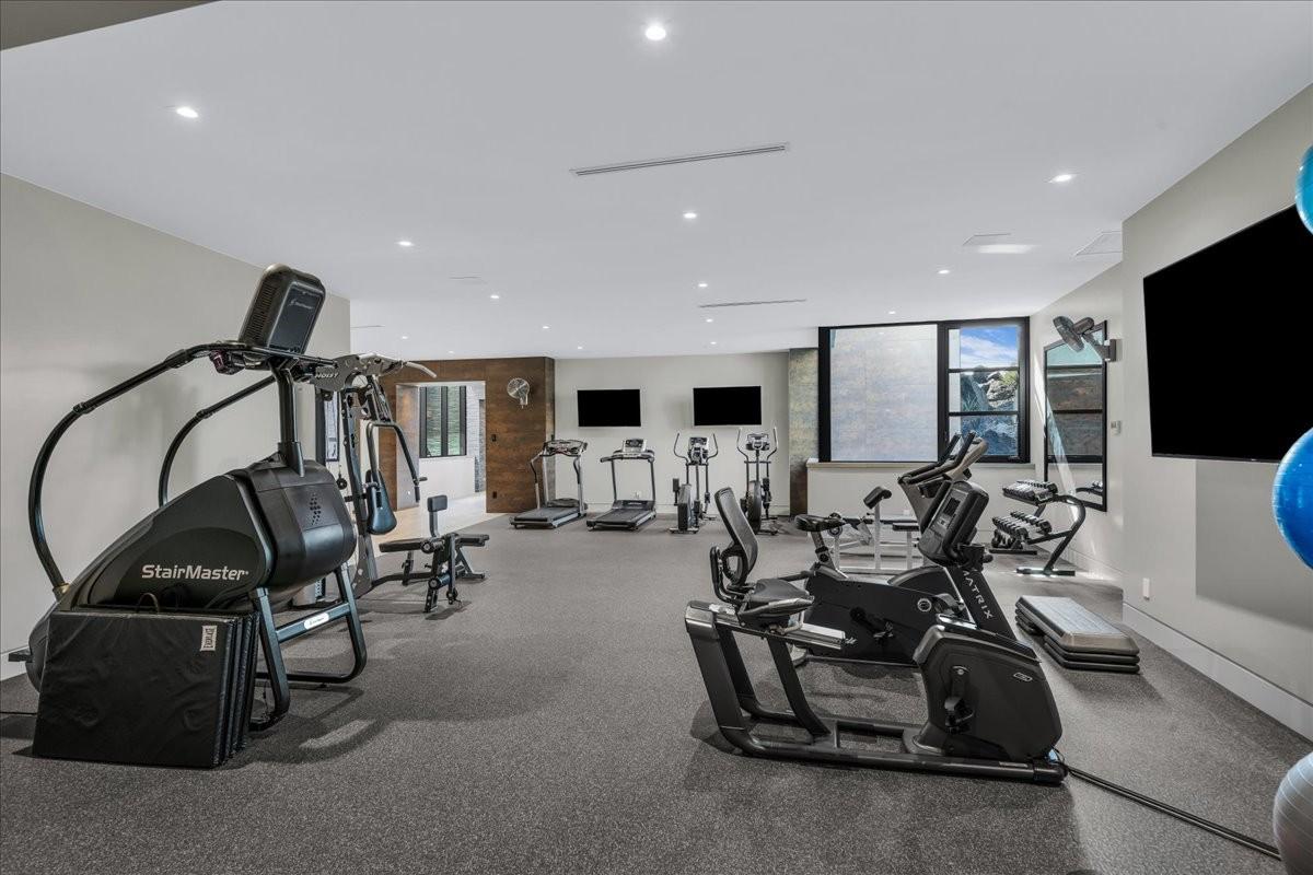 Dedicated fitness room featuring recessed lighting, durable rubber flooring, multiple flat-screen televisions, and large windows