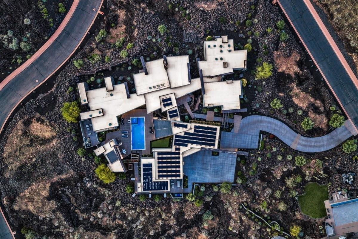 Architectural compound featuring multiple flat-roof structures, a central swimming pool, extensive solar panel arrays, and a winding paved pathway