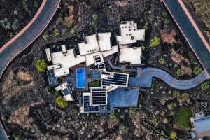 Architectural compound featuring multiple flat-roof structures, a central swimming pool, extensive solar panel arrays, and a winding paved pathway