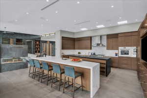 Spacious open-concept kitchen and living area featuring a large center island with waterfall countertop, a second island with integrated sink, wood-finish cabinetry, and a linear fireplace with stone surround
