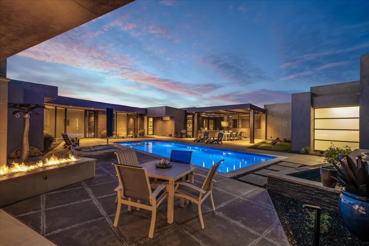 Contemporary outdoor living area featuring a rectangular pool with integrated spa, a fire pit, and a covered patio with an outdoor kitchen
