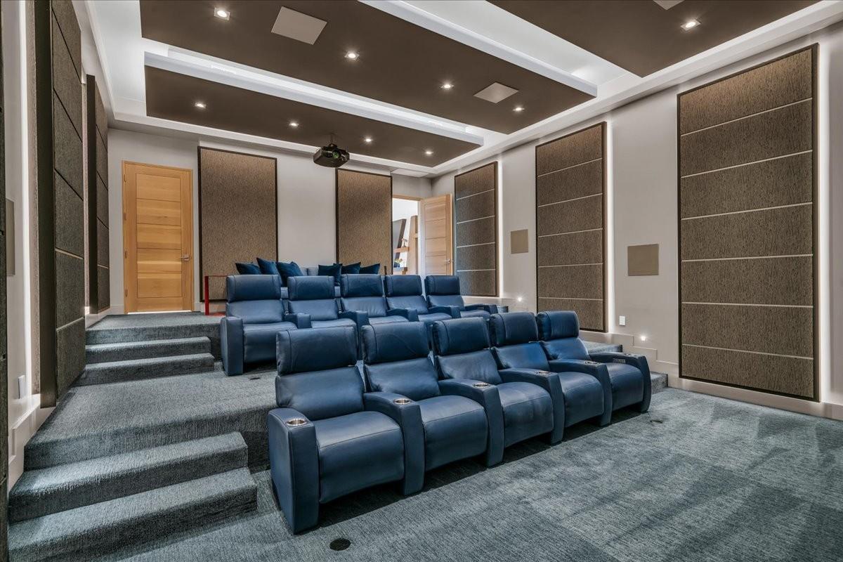 Dedicated media room featuring tiered seating, recessed ceiling lighting, wall-mounted acoustic panels, and a ceiling-mounted projector