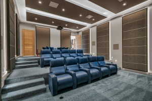 Dedicated media room featuring tiered seating, recessed ceiling lighting, wall-mounted acoustic panels, and a ceiling-mounted projector