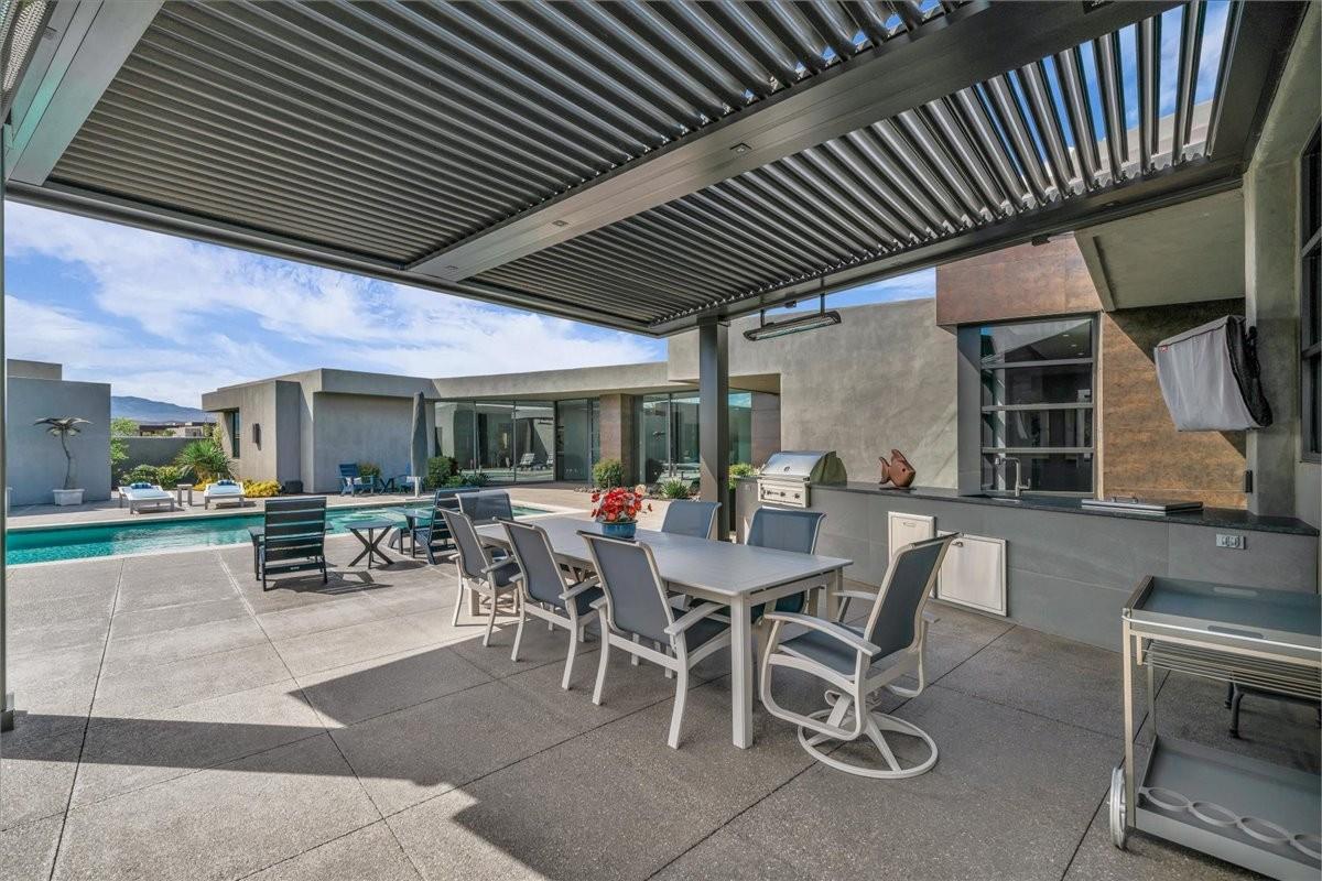 Covered outdoor living area featuring a louvered patio cover, built-in outdoor kitchen with grill, pool, and concrete patio