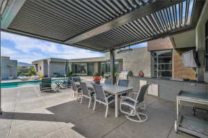 Covered outdoor living area featuring a louvered patio cover, built-in outdoor kitchen with grill, pool, and concrete patio