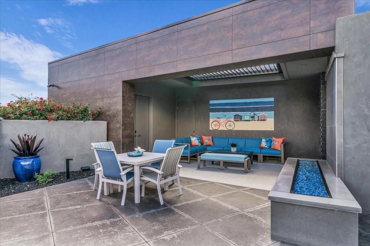 Spacious rooftop patio featuring large format tile flooring, a built-in fire pit with blue glass rocks, a covered lounge area, and raised planters