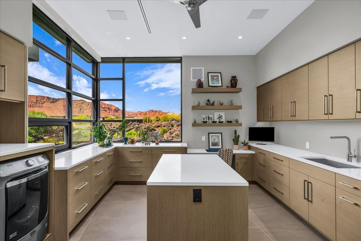 Contemporary utility space featuring expansive window walls, light wood-finish cabinetry, white countertops, a built-in sink with a gooseneck faucet, and a central island workspace