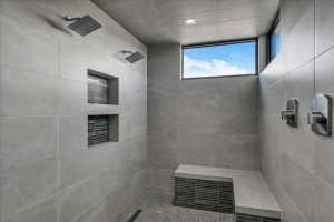 Spacious shower with two rainfall showerheads, a built-in bench, recessed display niches with mosaic tile accents, and a transom window