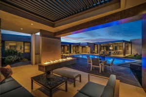 Expansive outdoor living area featuring a linear fire feature, a rectangular swimming pool, and a covered patio with recessed lighting