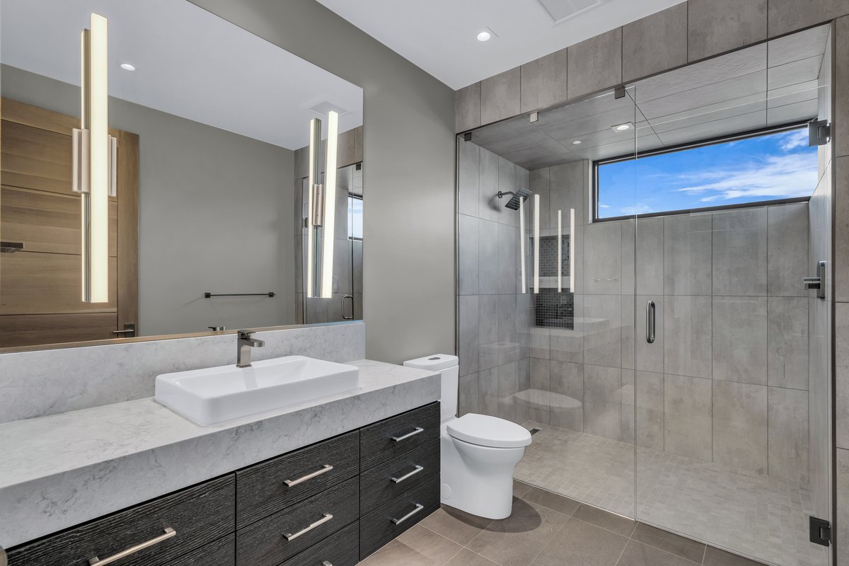 Modern bathroom featuring a spacious glass-enclosed shower with gray tiled walls and a high horizontal window