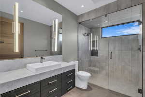 Modern bathroom featuring a spacious glass-enclosed shower with gray tiled walls and a high horizontal window