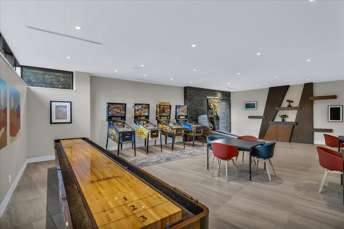 Spacious recreational room featuring light wood-finish flooring, recessed lighting, and a shuffleboard table