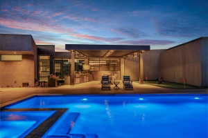 Illuminated swimming pool and integrated spa with a built-in outdoor kitchen under a covered patio