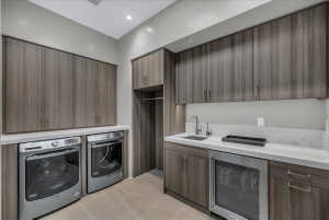 Utility room featuring extensive wood-finish cabinetry, light-toned countertops, a built-in sink with a gooseneck faucet, and a stainless steel under-counter refrigerator