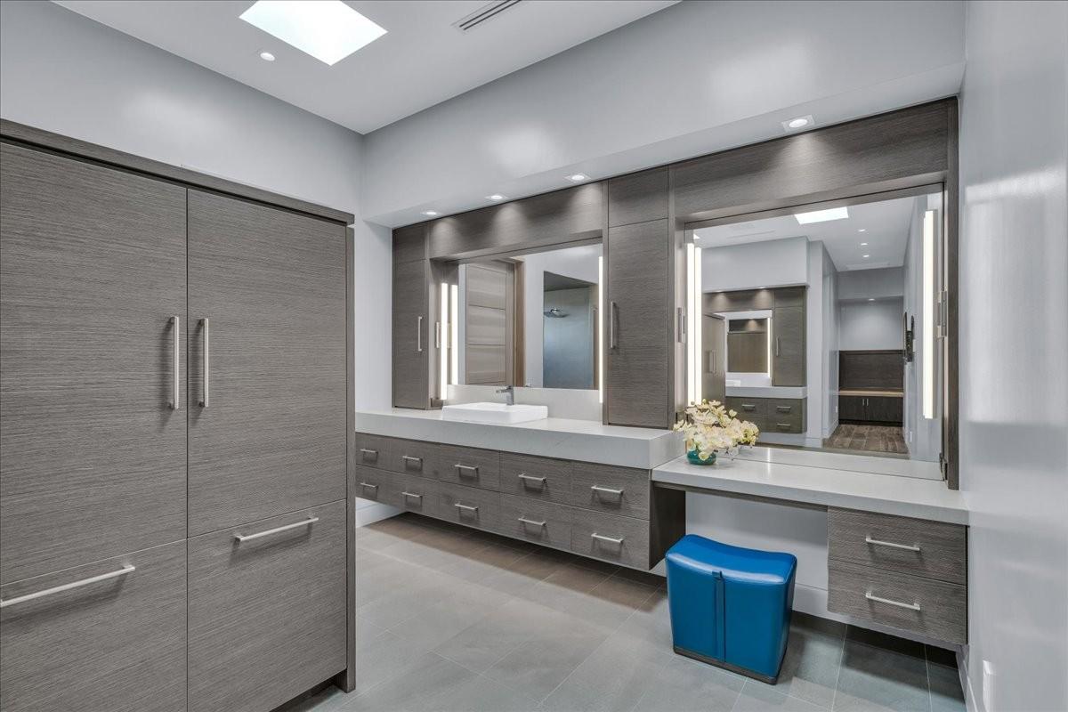 Spacious bathroom featuring extensive built-in cabinetry with wood-finish doors, integrated vanity lighting, dual vessel sinks, and a skylight