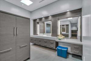 Spacious bathroom featuring extensive built-in cabinetry with wood-finish doors, integrated vanity lighting, dual vessel sinks, and a skylight