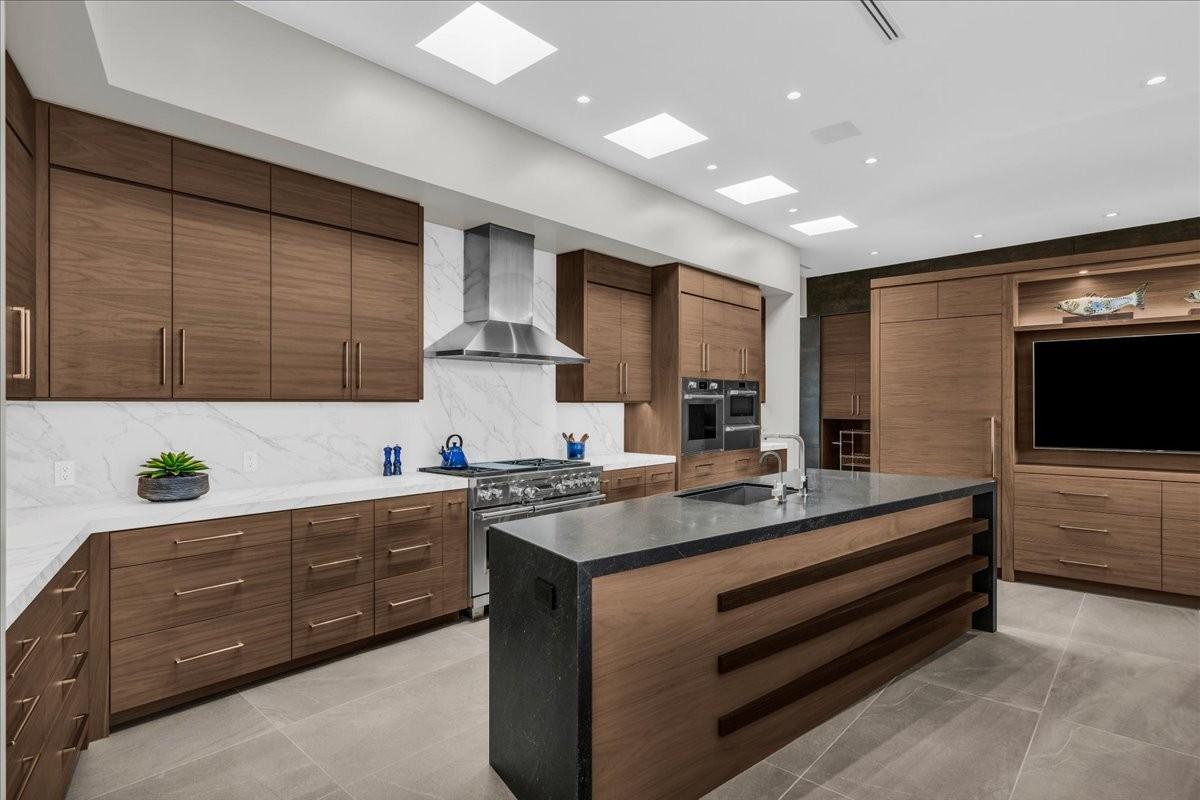 Modern kitchen featuring wood-finish cabinetry, white stone countertops, and a full-height stone backsplash