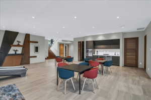 Spacious open area featuring wood-finish flooring, a contemporary wet bar with integrated appliances, recessed lighting, and a prominent wooden staircase