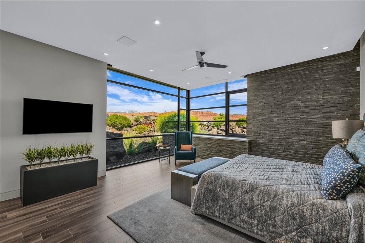Expansive floor-to-ceiling windows with black framing, wood-finish flooring, a contemporary ceiling fan, recessed lighting, and a textured stone accent wall