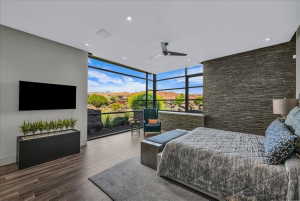 Expansive floor-to-ceiling windows with black framing, wood-finish flooring, a contemporary ceiling fan, recessed lighting, and a textured stone accent wall