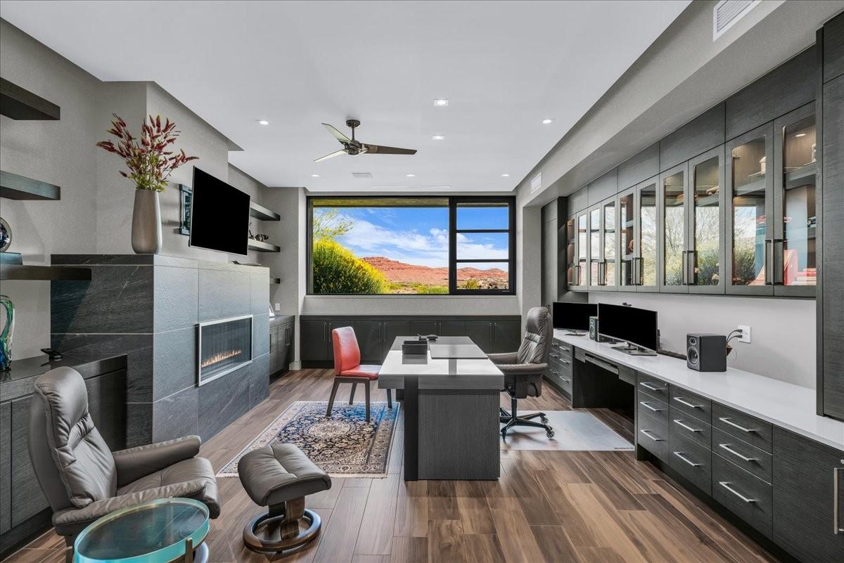 Modern office space featuring a linear fireplace with stone surround, wood-finish flooring, built-in desk, built-in cabinetry, and a large picture window