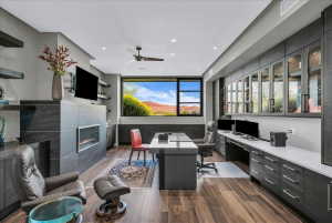 Modern office space featuring a linear fireplace with stone surround, wood-finish flooring, built-in desk, built-in cabinetry, and a large picture window