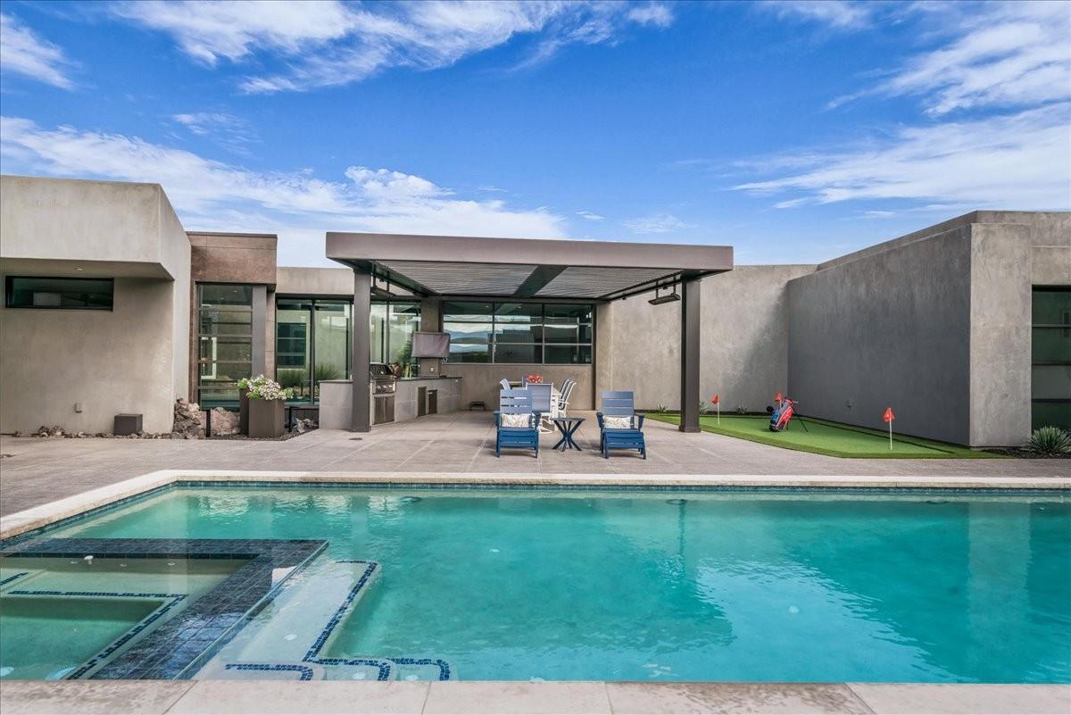 Backyard oasis featuring a rectangular swimming pool with integrated spa and steps, concrete patio, and a covered outdoor kitchen