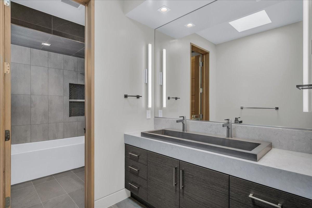 Contemporary bathroom featuring a dark wood-finish vanity with a light countertop, integrated rectangular sink, and dual wall-mounted faucets
