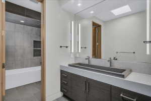 Contemporary bathroom featuring a dark wood-finish vanity with a light countertop, integrated rectangular sink, and dual wall-mounted faucets