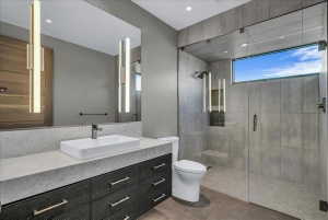 Modern bathroom featuring a frameless glass walk-in shower with a window, a single-basin vanity with a rectangular vessel sink, a stone-finish countertop, and dark wood-finish cabinetry