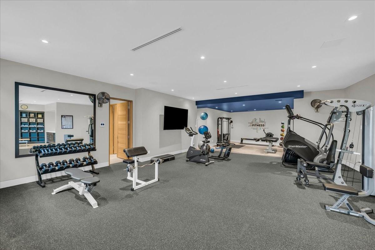 Spacious home gym featuring rubber flooring, recessed lighting, a large wall-mounted mirror, and an accent wall with a blue bulkhead