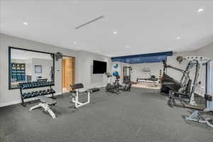 Spacious home gym featuring rubber flooring, recessed lighting, a large wall-mounted mirror, and an accent wall with a blue bulkhead