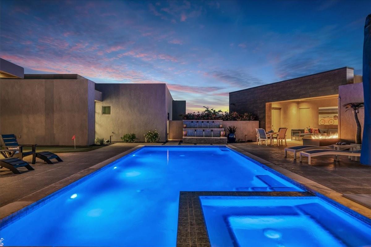 Illuminated swimming pool with integrated spa, surrounded by a paved patio