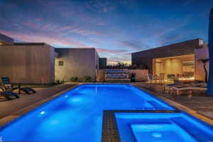 Illuminated swimming pool with integrated spa, surrounded by a paved patio