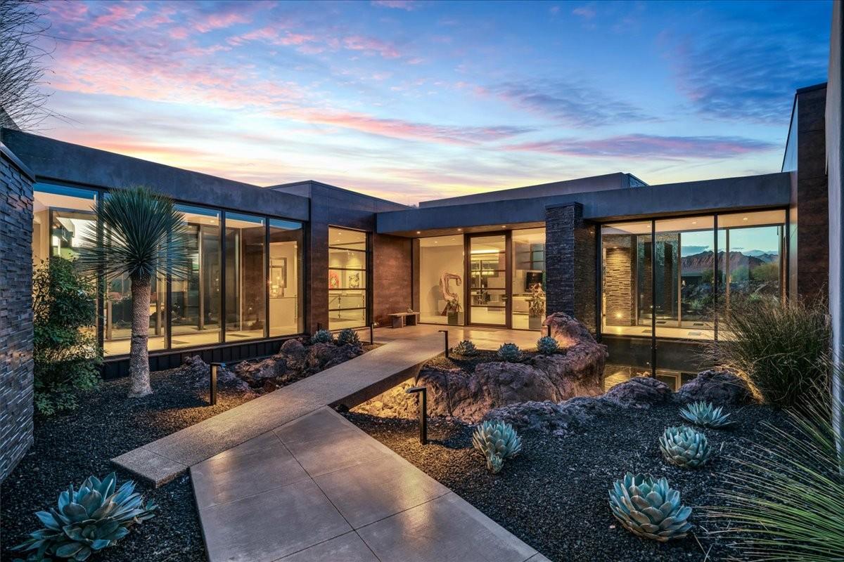 Contemporary architectural exterior with extensive floor-to-ceiling glass, stacked stone accents, a flat roofline, and integrated landscape lighting highlighting desert plantings