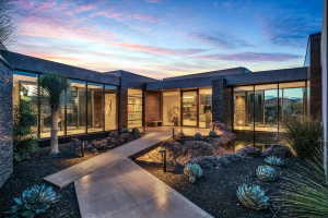 Contemporary architectural exterior with extensive floor-to-ceiling glass, stacked stone accents, a flat roofline, and integrated landscape lighting highlighting desert plantings