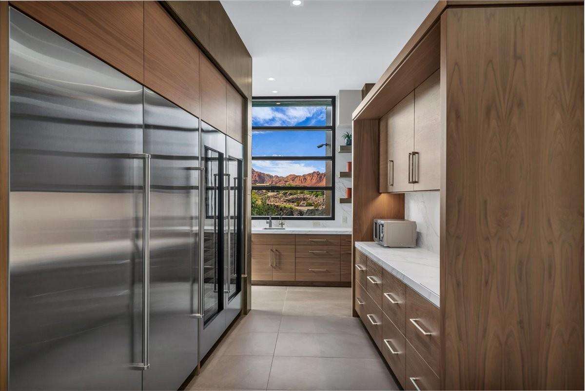 Contemporary kitchen featuring integrated stainless steel appliances, custom wood cabinetry, a built-in beverage refrigerator, and a window with mountain scenery