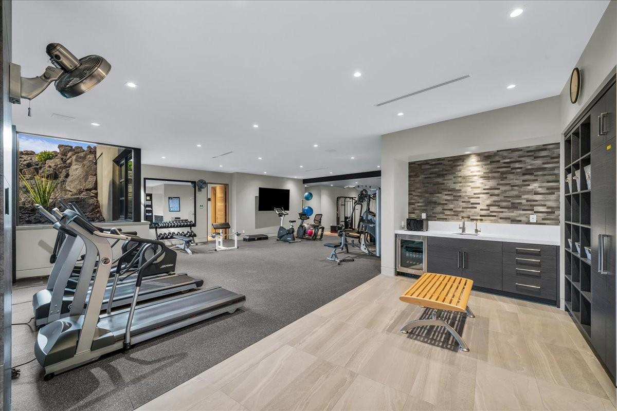 Dedicated fitness room featuring recessed lighting, a rock wall backdrop, a built-in wet bar with a beverage cooler, and a built-in storage system