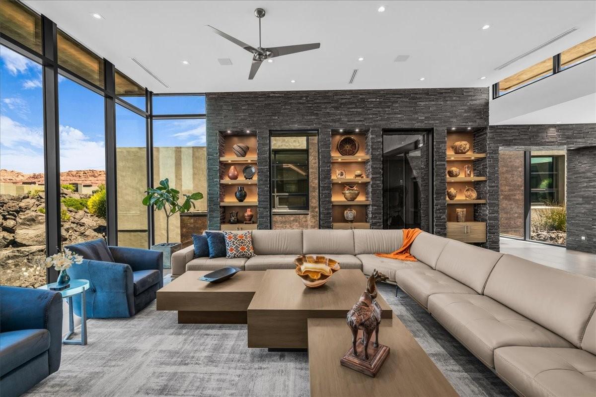 Spacious living area featuring floor-to-ceiling windows, a textured stone accent wall with integrated shelving, recessed lighting, and a modern ceiling fan