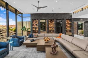 Spacious living area featuring floor-to-ceiling windows, a textured stone accent wall with integrated shelving, recessed lighting, and a modern ceiling fan
