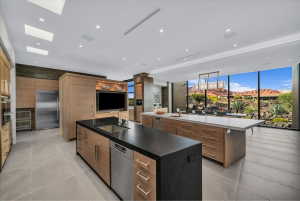 Open-concept kitchen and dining area featuring dual islands with stone countertops, integrated stainless steel appliances, extensive wood cabinetry, and floor-to-ceiling windows overlooking a desert landscape