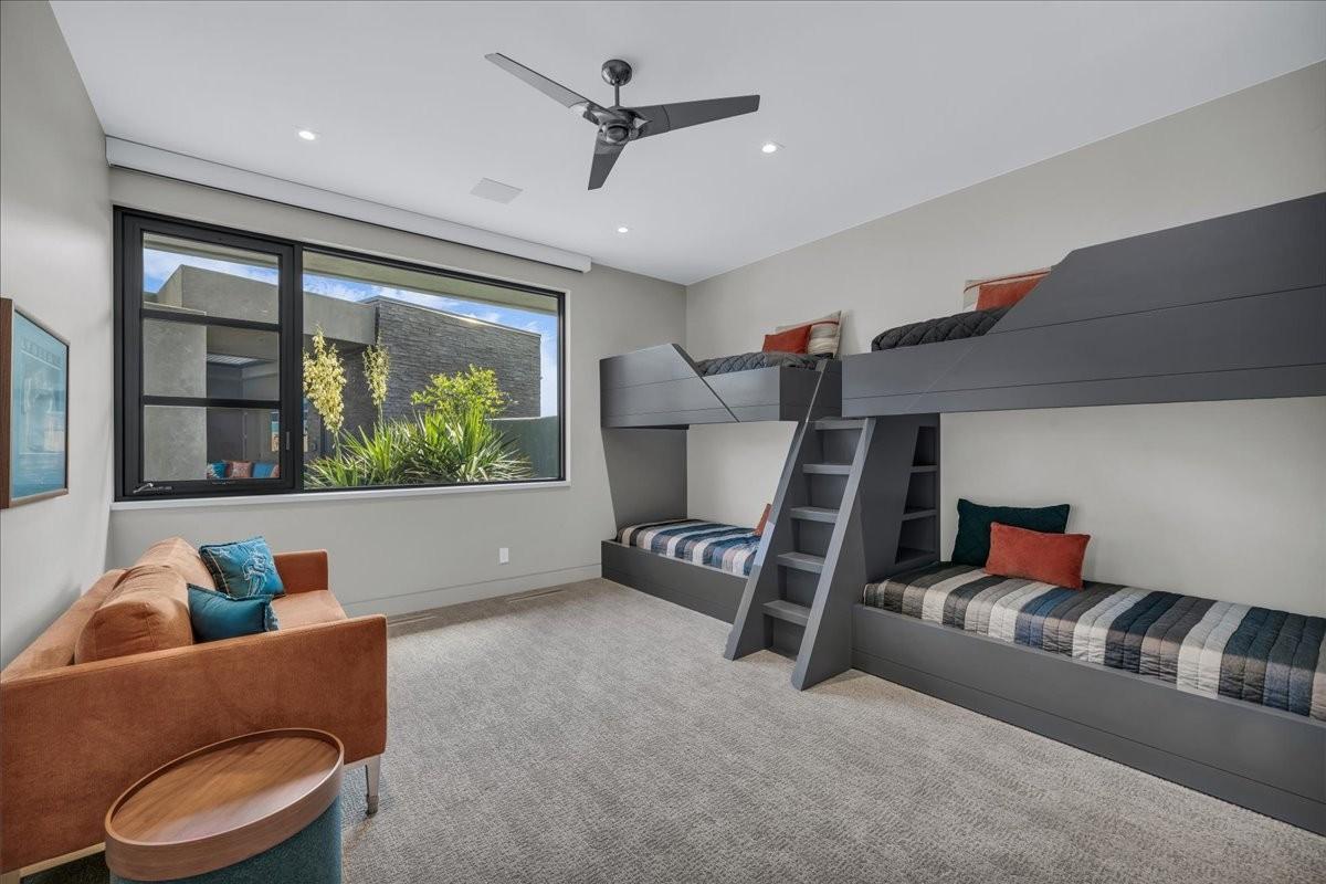 Spacious room featuring a large window overlooking exterior landscaping, built-in bunk beds with integrated ladders and shelving, recessed lighting, and a ceiling fan