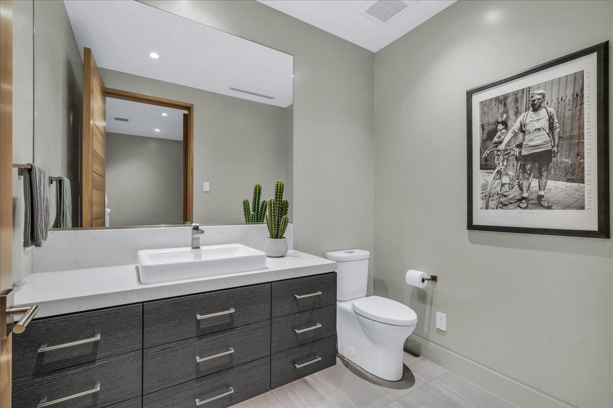 Modern powder room featuring a rectangular vessel sink, a light-toned countertop, a dark wood-finish vanity with ample storage, a large wall-mounted mirror, and tile flooring